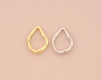 以下が含まれることがあります： 柔らかいピンク色の背景に、金色のものと銀色のもの、2つのしずく型の留め金が表示されています。留め金は有機的で質感のある外観をしており、手作りまたは自然なデザインを示唆しています。ジュエリーやアクセサリーに使用される可能性が高いです。