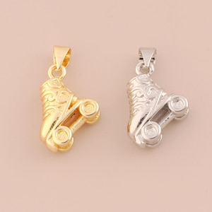 Puede incluir: Dos colgantes de patines, uno dorado y otro plateado, sobre un fondo rosa pálido. Los colgantes presentan intrincados adornos y pequeñas ruedas, evocando un tema vintage o retro.