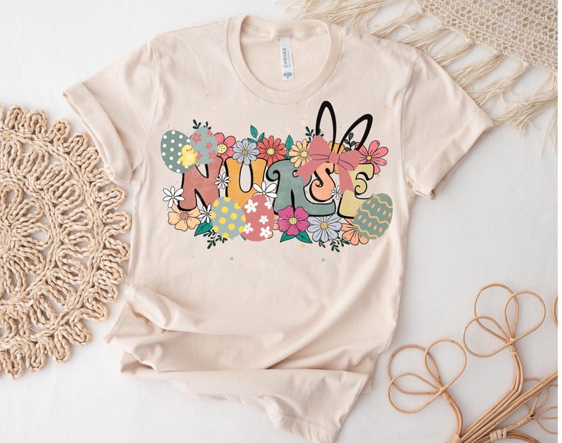 May include: A beige t-shirt with a graphic design of the word "NURSE" surrounded by colorful flowers and Easter eggs. The graphic also includes a bunny rabbit with a pink bow.