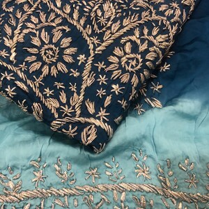 May include: A fabric textile featuring an ombre gradient from deep navy blue to light teal. The navy section is densely embroidered with metallic gold floral and vine patterns, while the lighter teal section features a horizontal border of gold.