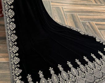 Puede incluir: Un chal de terciopelo negro con intrincados bordados dorados en los bordes. Los detallados patrones florales y de cachemira crean un diseño lujoso y elegante. El chal está drapeado, mostrando su tejido fluido y sus adornos.