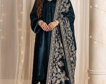 May include: A dark teal velvet long-sleeved tunic and matching trousers paired with a coordinating shawl featuring intricate gold embroidery along the borders. The ensemble is accessorized with a multi-strand pearl necklace and matching hand jewelry.