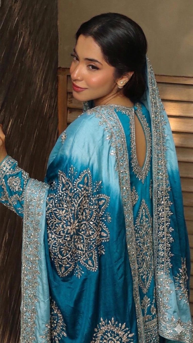 May include: A vibrant turquoise and sky blue ombre tunic featuring intricate silver metallic embroidery in floral and geometric patterns. The garment includes long sleeves, a teardrop-shaped back cutout, and a matching draped shawl overlay.