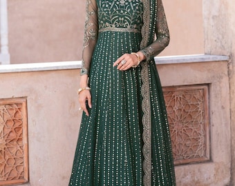 May include: A dark green formal gown with long sleeves and intricate gold embroidery on the bodice and sleeves. The dress features a flowing skirt and a matching scarf, creating an elegant silhouette. The gown is adorned with small, sparkling accents.