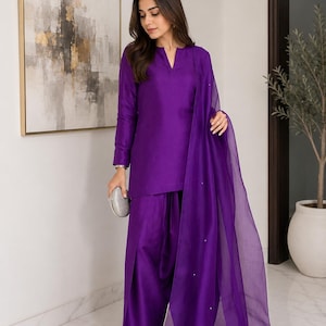 May include: A vibrant purple ensemble consisting of a long-sleeved tunic with a notched neckline and matching loose-fitting trousers. The outfit is paired with a sheer, lightweight purple dupatta featuring small, evenly spaced embellishments.