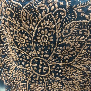 May include: A deep teal fabric featuring an intricate, large-scale floral pattern embroidered with metallic gold thread. The design consists of dense, repeating petal and leaf motifs radiating from a central circular element in a symmetrical layout.