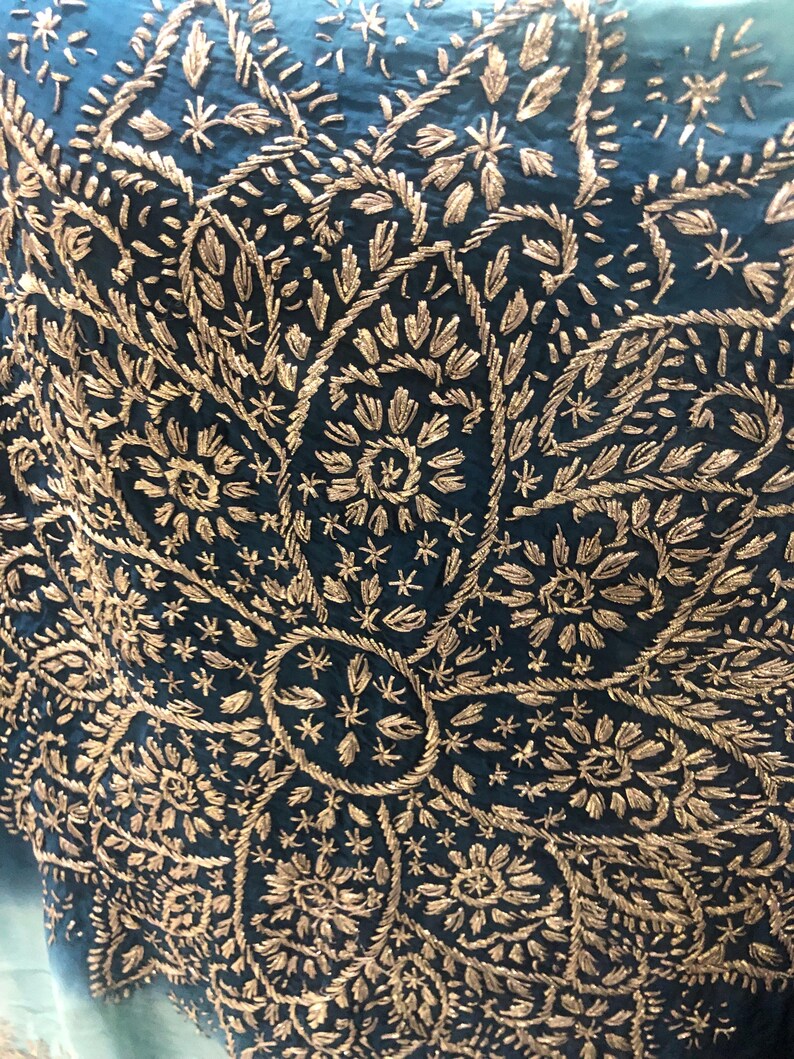 May include: A deep teal fabric featuring an intricate, large-scale floral pattern embroidered with metallic gold thread. The design consists of dense, repeating petal and leaf motifs radiating from a central circular element in a symmetrical layout.