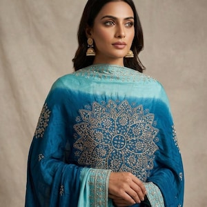 May include: A teal and turquoise ombre shawl featuring intricate gold-toned embroidery in a large central mandala pattern and a detailed border. The fabric transitions from a lighter shade at the top to a deeper blue at the bottom edge.