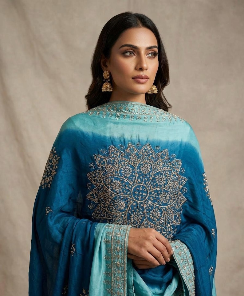 May include: A teal and turquoise ombre shawl featuring intricate gold-toned embroidery in a large central mandala pattern and a detailed border. The fabric transitions from a lighter shade at the top to a deeper blue at the bottom edge.