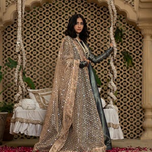 May include: A woman wearing a dark gray and silver embellished gown with a matching sheer shawl. The shawl is adorned with sequins. The background features a decorative swing and a floor covered in red rose petals.