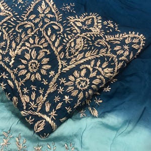 May include: A fabric textile featuring an ombre gradient from deep teal to light turquoise. The fabric is adorned with intricate gold-colored thread embroidery in floral and leaf patterns, concentrated in a dense border design.