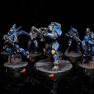 May include: Miniature figurines of futuristic soldiers in blue and gold armor, each holding a weapon. The figures are posed on circular bases with orange accents, set against a black background. The collection includes various action poses.