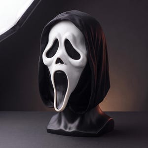 May include: A white plastic ghost mask with elongated black eye sockets and a wide, open black mouth, attached to a black fabric hood that drapes over the head and shoulders, displayed on a black mannequin head bust for clear visibility.