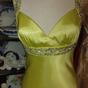 May include: A lime green formal dress with a V-neckline and embellished straps. The bodice features a beaded band at the waist. The dress is displayed on a mannequin.