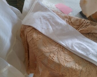 May include: White long gloves with small white pearl embellishments. The gloves are lying on a beige lace fabric.