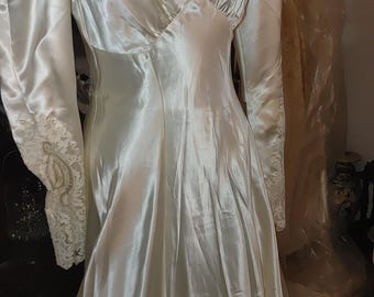 May include: Ivory satin wedding dress with long sleeves and a fitted bodice. The dress features a V-neckline with delicate lace trim and lace detailing on the cuffs. The skirt flows into a subtle train.