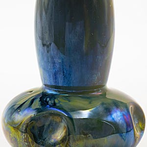 Könnte beinhalten: Eine Keramikvase mit bauchigem Fuß und zylindrischem Hals, die eine glänzende, irisierende Glasur aufweist, welche tiefe Blau-, Grün- und Goldtöne mit subtilen metallischen Akzenten und einer glatten, reflektierenden Oberfläche kombiniert.