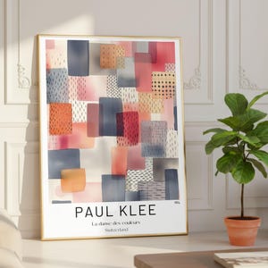 以下が含まれることがあります： ピンク、オレンジ、青、グレーの色合いで重なり合う長方形の抽象的なデザインが特徴の、額装されたアートプリントです。「PAUL KLEE」と「La danse des couleurs Switzerland」の文字が含まれています。明るい部屋に飾られています。