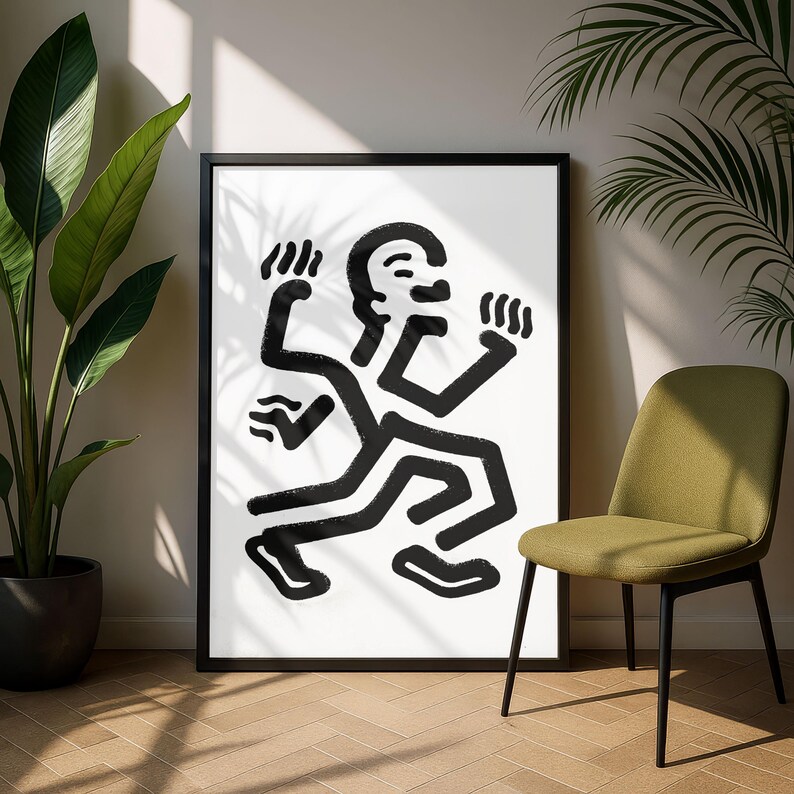 Puede incluir: Impresi&oacute;n art&iacute;stica abstracta en blanco y negro de una figura con brazos y piernas extendidos. La obra de arte est&aacute; enmarcada en un marco negro y se muestra sobre un fondo blanco. Una silla verde y plantas en macetas est&aacute;n en el fondo.