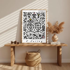 May include: A framed art print featuring a black and white abstract design with the word "SUMMER" at the top. The artwork includes two stylized figures and the artist's signature, "K. Haring". The print is displayed on a wooden bench.