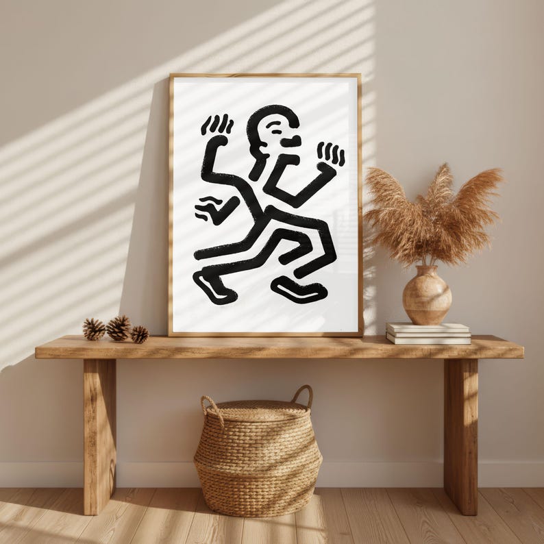 Puede incluir: Una impresi&oacute;n art&iacute;stica enmarcada que presenta una figura abstracta en blanco y negro con m&uacute;ltiples extremidades. La obra de arte se exhibe en un banco de madera con una cesta tejida, un jarr&oacute;n y plantas secas. La habitaci&oacute;n tiene una paleta de colores neutros.