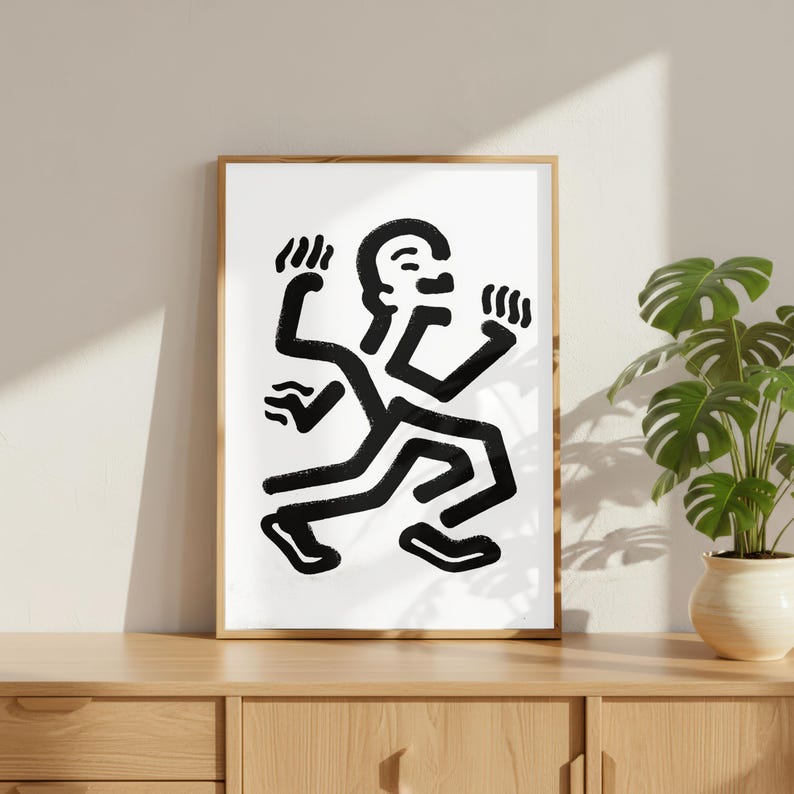 Puede incluir: Una impresi&oacute;n art&iacute;stica enmarcada que presenta una figura abstracta en blanco y negro en movimiento. La obra de arte representa una persona estilizada con m&uacute;ltiples brazos y piernas, sobre un fondo blanco. El marco es de color marr&oacute;n claro y la impresi&oacute;n se exhibe en un mueble de madera.