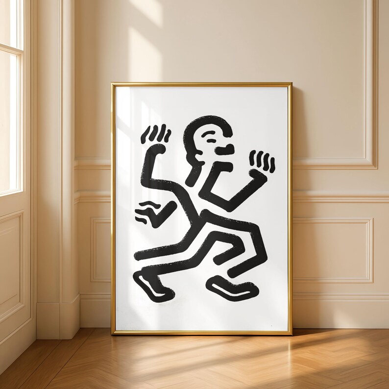 Puede incluir: Una impresi&oacute;n art&iacute;stica enmarcada con una figura abstracta en blanco y negro en movimiento. La obra de arte tiene un estilo minimalista con l&iacute;neas gruesas y audaces. El marco dorado a&ntilde;ade un toque de elegancia al dise&ntilde;o moderno, adecuado para la decoraci&oacute;n del hogar.