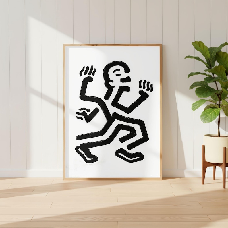 Puede incluir: Una impresi&oacute;n art&iacute;stica enmarcada que presenta una figura abstracta en blanco y negro en una pose din&aacute;mica. La obra de arte tiene l&iacute;neas gruesas y audaces y un estilo minimalista. El marco es de color madera clara, y la impresi&oacute;n se muestra contra una pared blanca.