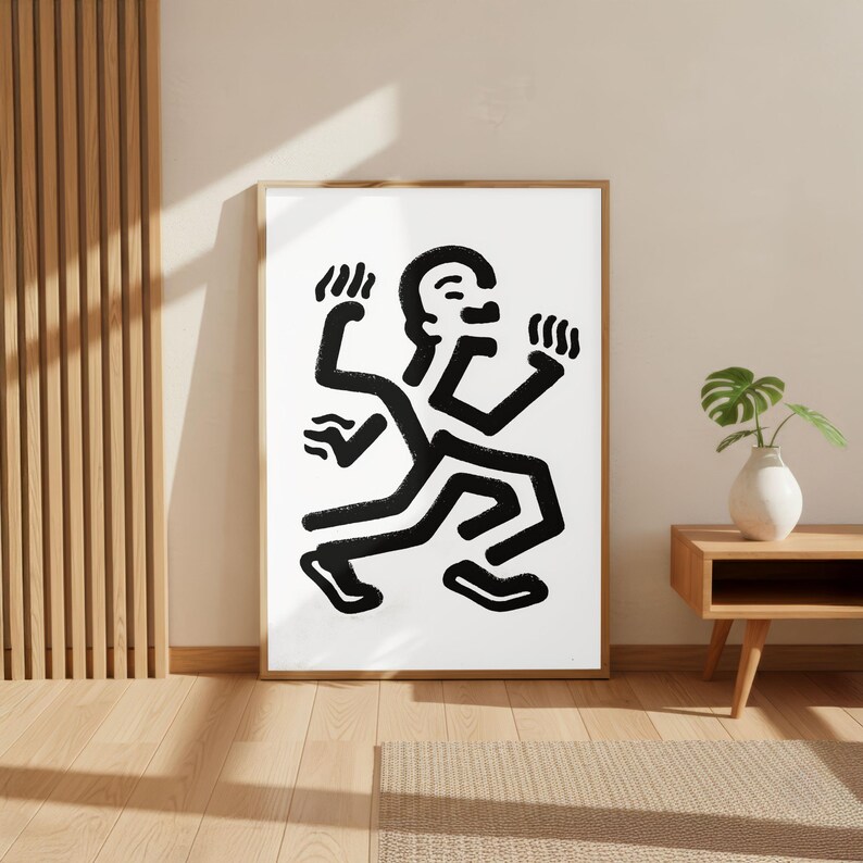 Puede incluir: L&aacute;mina de arte abstracto en blanco y negro que representa una figura estilizada en movimiento. La obra de arte tiene un dise&ntilde;o minimalista con l&iacute;neas negras gruesas sobre un fondo blanco, enmarcada en un marco de madera natural. La figura parece estar bailando o corriendo.