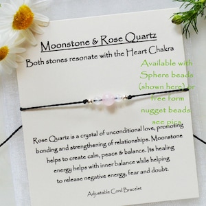 May include: A black adjustable cord bracelet with a rose quartz and moonstone bead. The card reads "Moonstone & Rose Quartz" and "Both stones resonate with the Heart Chakra".