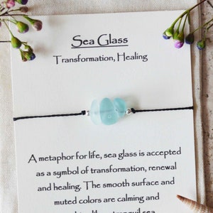 May include: A blue sea glass charm on a black adjustable cord bracelet. The card reads "Sea Glass Transformation, Healing" and "A metaphor for life, sea glass is accepted as a symbol of transformation, renewal and healing. The smooth surface and muted colors are calming and soothing like a tranquil sea. Adjustable Cord Bracelet."