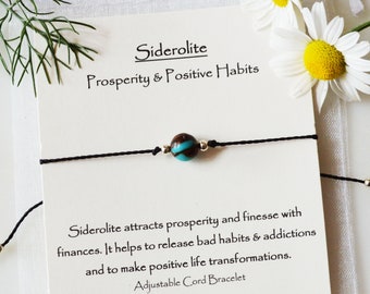 May include: A black adjustable cord bracelet with a brown and turquoise bead. The card reads "Siderolite Prosperity & Positive Habits" and describes the stone's properties.
