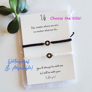 May include: A pair of matching black and white friendship bracelets with compass charms, displayed on a card with the text "Us". The card also includes the phrases "No matter where we are" and "I love you!"