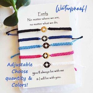 May include: Five adjustable woven bracelets in black, navy, light blue, pink, and white. Each bracelet features a gold-colored compass charm. The bracelets are displayed with a card that reads "Family" and "Waterproof!"