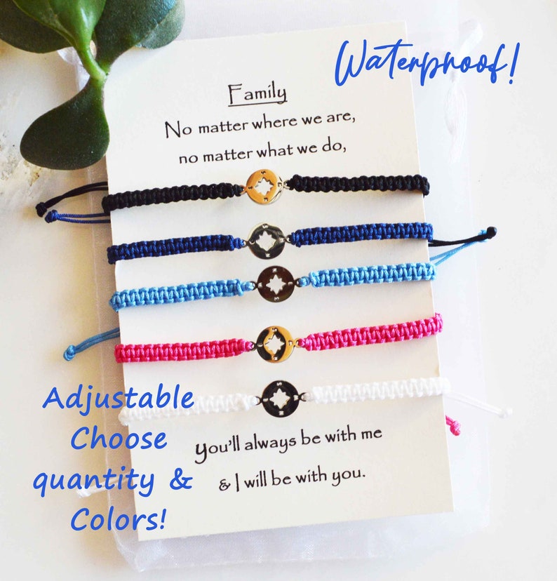 May include: Five adjustable woven bracelets in black, navy, light blue, pink, and white. Each bracelet features a gold-colored compass charm. The bracelets are displayed with a card that reads "Family" and "Waterproof!"
