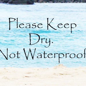 Pu&ograve; includere: Un cartello con il testo "Please Keep Dry. Not Waterproof" su uno sfondo di acqua blu e sabbia bianca.