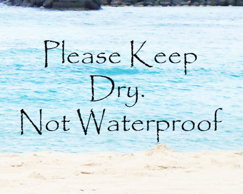 Pu&ograve; includere: Un cartello con il testo "Please Keep Dry. Not Waterproof" su uno sfondo di acqua blu e sabbia bianca.
