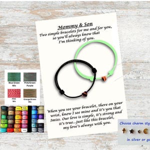 May include: Two adjustable cord bracelets, one black and one light green, each featuring a small heart charm. They are displayed on a white card with the text Mommy & Son, Two simple bracelets for me and for you, so you'll always know that I'm thinking of you.