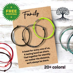 May include: Family friendship bracelets with a green, black, and red string. The bracelets have silver beads and are tied together with a knot. The card says "Family" and "A bead for every one of us, A lasting bond we share, Tied together for eternity no matter the distance, we'll always be there."  20+ colors!