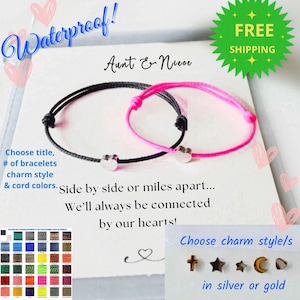 May include: Two matching bracelets, one black and one pink, each with a heart charm. The image includes text that says "Waterproof!" and "Aunt & Niece". The bracelets are described as "Side by side or miles apart... We'll always be connected by our hearts!"
