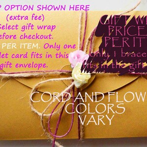 Pu&ograve; includere: Una busta dorata con un fiocco di spago marrone e un fiore rosa. Il testo sulla busta recita "Gift Wrap Option Shown Here (extra fee) Select gift wrap before checkout. Price is PER ITEM. Only one bracelet card fits in this gift envelope. Gift Wrap Price is Per Item Only 1 bracelet card fits in the gift envelope Cord and Flower Colors Vary".