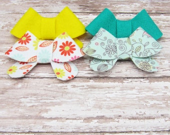 May include: Three felt fabric bows, one yellow, one teal, and one with a floral pattern in shades of blue, pink, and green.