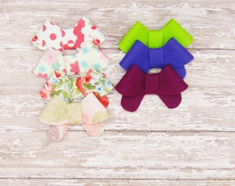 May include: Five fabric bows in various colors and patterns. The bows are arranged in a stack, with the largest bow on the bottom and the smallest bow on top. The bows are made of a soft, textured fabric and have a simple, elegant design.