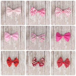 Könnte beinhalten: Neun Stoff-Haarschleifen in verschiedenen Rosa- und Rottönen, mit Mustern wie Tupfen, Blumen und Karos. Die Schleifen sind auf einem hellen Holzmaserung-Hintergrund angeordnet, um ihre verschiedenen Designs und Farben zu präsentieren.