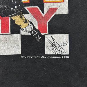 May include: Black t-shirt with a graphic design featuring the word "CITY" in red and white block letters. The design includes a stylized illustration of a person in athletic gear. The copyright reads "Copyright David James 1996".