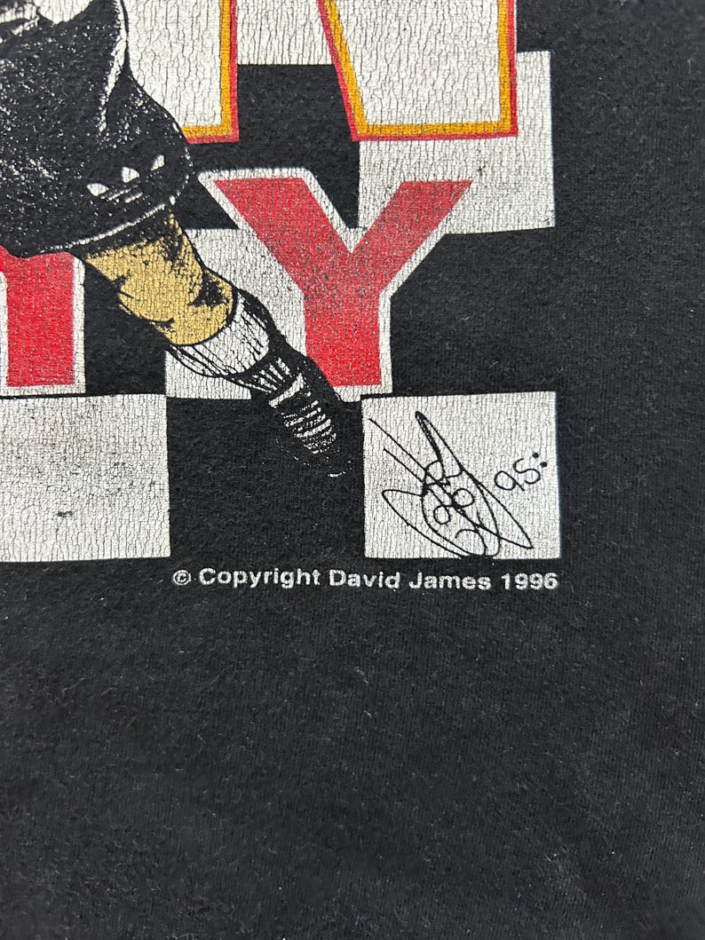 May include: Black t-shirt with a graphic design featuring the word "CITY" in red and white block letters. The design includes a stylized illustration of a person in athletic gear. The copyright reads "Copyright David James 1996".