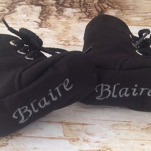 May include: A pair of black baby booties with the name "Blaire" embroidered on each in silver thread.