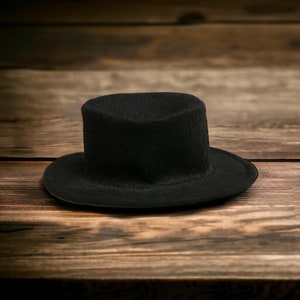 May include: A black top hat with a wide brim sits on a wooden surface.