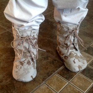May include: A pair of tan camouflage print ankle boots with laces. The boots are made of a soft, canvas-like material and have a rounded toe.