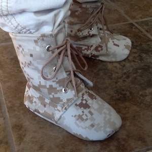 May include: A pair of tan camouflage ankle boots with laces. The boots are made of a canvas-like material and have a low heel.